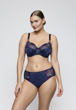 Woman wearing matching navy blue lace bra and panties with floral embroidery, standing against a plain light background.