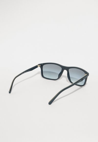 Μαύρα ορθογώνια γυαλιά ηλίου με βαθμιαία γκρι φακούς, διαθέτοντας λείες πλαστικές σκελίδες και λεπτούς βραχίονες με διακριτικά μεταλλικά στοιχεία.