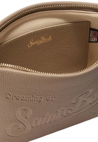 Sacoche en cuir beige avec un texte en relief "Rêvant de Saint Barth" et une poche intérieure. Comprend une fermeture éclair et une surface texturée.