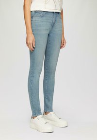 Jasnoniebieskie wąskie jeansy z denimu, charakteryzujące się klasycznym pięciopocketowym wzorem i dopasowanym krojem, w połączeniu z białymi sneakersami na platformie.