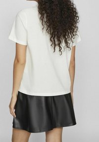 Camiseta de algodón blanca de manga corta, combinada con una falda corta de cuero sintético negra. El conjunto presenta un corte relajado y una textura suave.