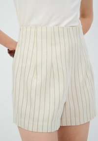 Pantaloni corti di colore crema con sottili righe verticali, realizzati in tessuto leggero. Presentano un'alta vita e tasche laterali per una maggiore comodità.