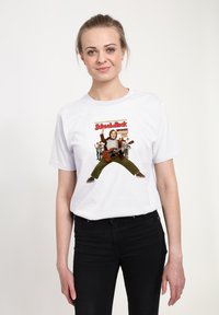 Mladá žena v bílem tričku s potiskem "School of Rock" zobrazujícím postavu hrající na kytaru a skupinu dětí v pozadí, černé kalhoty.