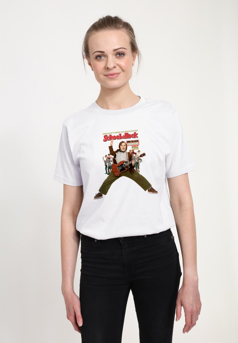 Mladá žena v bílem tričku s potiskem "School of Rock" zobrazujícím postavu hrající na kytaru a skupinu dětí v pozadí, černé kalhoty.