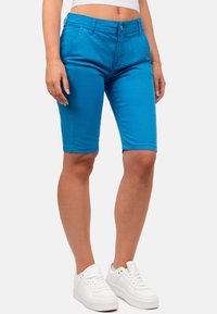 Bermuda in cotone blu con vestibilità slim, chiusura a bottone e tasche. Abbinati a scarpe da ginnastica bianche.