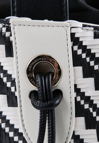 Woven czarno-biała torebka, z gładką białą skórzaną klapą, okrągłym metalowym oczkiem i czarnym sznurkiem.