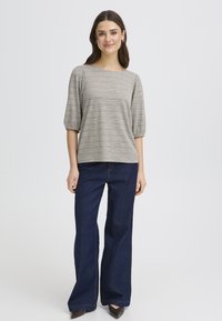 Haut à carreaux gris et blanc avec un large décolleté et des manches jusqu'au coude, associé à un jean évasé bleu foncé et des chaussures à talons marron.