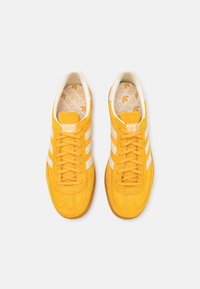 Gula mockaskor med vita ränder, med snörningsdesign och en texturerad gummisula. Innervadden har en mönstrad design.