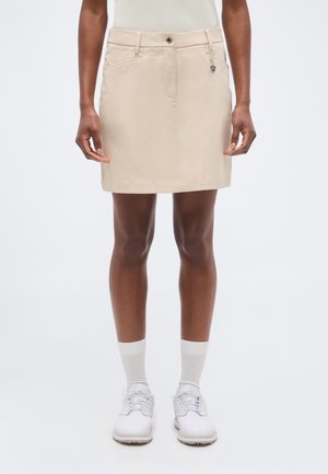 Beige knee-length skirt worn with white socks and white lace-up shoes on a standing person against a plain background.