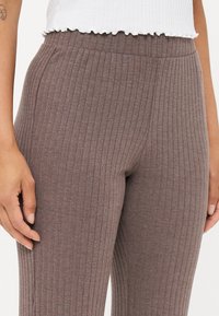Geribbelde bruine leggings met een elastieke tailleband, met een zachte textuur en een aansluitende pasvorm. Close-up afbeelding die de stofdetails en de fit laat zien.