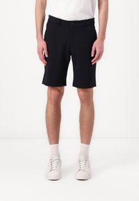 Black shorts made of a smooth fabric, featuring a button closure and belt loops. Paired with white sneakers and ankle-length socks.