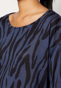 Blå- och svart randig topp med bred halsringning, i avslappnad passform och mjukt material. Tyget har en subtil lyster.