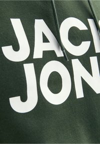 Gros plan sur un tissu vert foncé avec de grandes lettres blanches formant une partie de « JACK JONES » et un cordon de capuche vert foncé.