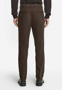 Bruna byxor med en skräddarsydd passform, med två bakfickor med knäppning, och ett slätt, texturerat tyg, tillsammans med svarta skor.