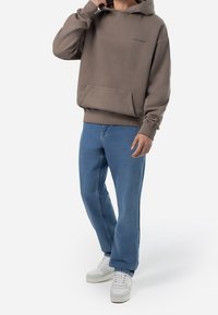 Brun huva tröja med framficka, kombinerad med ljusblå raka jeans och vita sneakers, som visar en avspänd outfit.