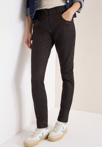 Mörkbruna slim-fit byxor med framfickor, som är kombinerade med beiga sneakers med ljusblå accenter. Slät textur och modern design.