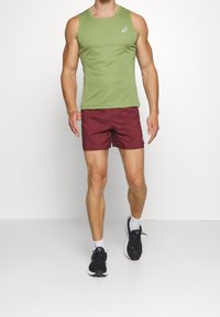 Top sin mangas verde, pantalones cortos burdeos, zapatillas negras con suelas blancas. Tela suave con un diseño ajustado, estilo atlético.