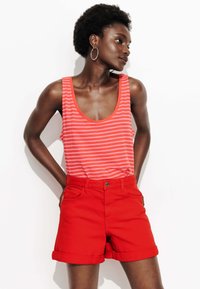 Shorts en denim rouge avec des revers et une fermeture à bouton, accompagnés d'un débardeur à rayures roses et blanches avec un décolleté bateau.