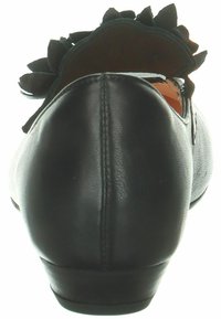 Schwarze Leder-Schuh mit runder Zehenpartie, ausgestattet mit einem dekorativen schwarzen Stoffakzent an der Ferse. Glatte Textur und flaches Sohlen-Design.