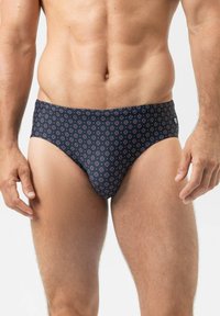 Heren zwemslips in marineblauw met een herhalend cirkelpatroon in rood en wit. Gemaakt van rekbaar materiaal, voorzien van een mid-rise ontwerp en een elastische tailleband.