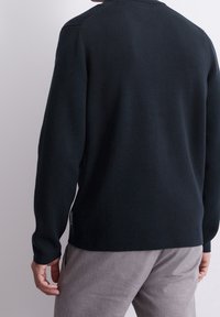 Maglione lavorato a maglia blu navy con scollo rotondo e maniche allungate, caratterizzato da una leggera texture e un piccolo logo etichetta all'orlo.