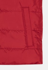Rød polstret jakke-seksjon med en synlig lomme, som har en glatt, blank tekstur og horisontal quiltet design.