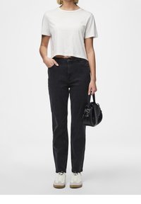 Svarta denimjeans med hög midja, kombinerat med en vit kort topp. Bärs med vita sneakers och en liten svart handväska.