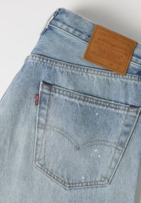 Jean en denim Levi's bleu clair montrant une poche arrière avec surpiqûres orange, étiquette rouge Levi's et patch en cuir marron sur la ceinture.