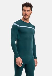 Długi rękaw sportowej koszulki w ciemnym odcieniu zieleni morskiej, z jasnoniebieskim poziomym paskiem na wysokości klatki piersiowej oraz fakturowaną tkaniną. Dopasowany krój.