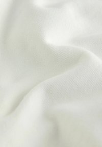 Tissu blanc doux avec une texture en tricot fin et de légers plis créant des ombres et des reflets subtils.