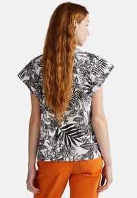 Blusa de manga corta en tejido blanco con estampado de hojas tropicales negras; corte holgado con dobladillo recto, combinada con pantalones naranjas.