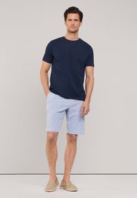 T-shirt à manches courtes bleu marine associé à un short rayé bleu et blanc, avec une coupe décontractée et un tissu doux. Chaussures à enfiler marron clair.