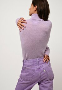 Maglione a collo alto lilla con lavorazione a maglia morbida e testurizzata e maniche lunghe; abbinato a jeans a vita alta di un delicato colore viola chiaro con tasche posteriori.