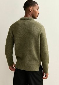 Olivgrön stickad tröja med texturerad yta, utrustad med ribbad krage och muddar, designad med vida ärmar och avslappnad passform.