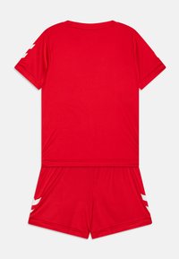 Ensemble de sport rouge comprenant un haut à manches courtes avec un col rond et un short. Accentué de rayures diagonales blanches sur les manches et le short.