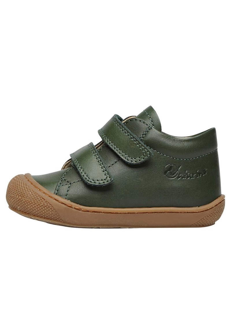 Scarpa in pelle verde con due cinturini in Velcro, punta arrotondata e suola in gomma marrone. Caratterizzata da dettagli di cucitura e un cappuccio della punta texture.