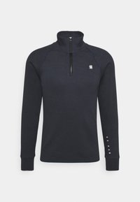 Marinblå fleecepullover med hög krage och halvdragkedja. Har långa raglanärmar och diskret logotyp på bröstet och ärmen.