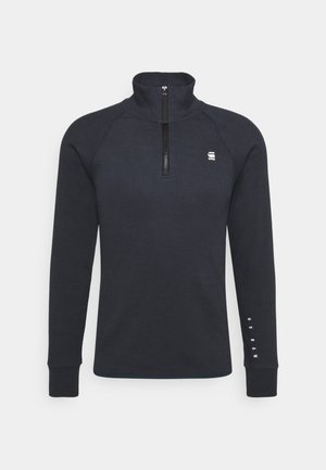 Námořnický fleecový pulovr s vysokým límcem a designem na poloviční zip. Obsahuje dlouhé raglánové rukávy a decentní branding na hrudi a rukávu.