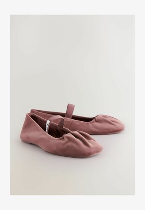 Șlapi roz din suede, cu vârful rotund, detalii pliate în față și o curea la spate pentru susținere. Talpă plată cu accente minime.