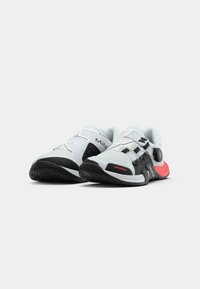 White athletic shoes with black accents, textured mesh upper, flexible sole, and adjustable straps for fit. Red detail at heel.
