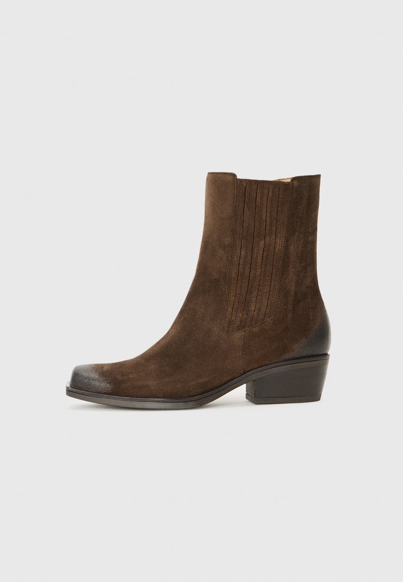 Stivaletto in suede marrone con punta arrotondata, dettagli verticali testurizzati e tacco basso a blocco. Finiture nere lucide sulla punta.