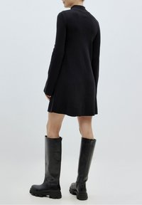 Robe noire en tricot à manches longues avec un col structuré, associée à de grandes bottes en cuir noir à semelles épaisses et fermetures éclair latérales.