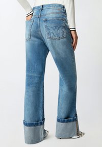 Svijetloplave traperice širokih nogavica, s kontrastnim obrubom i ukrasnim šavovima na stražnjim džepovima.