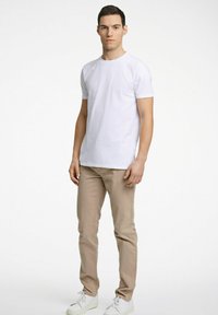Vit kortärmad t-shirt med rund halsringning, i kombination med khaki chinos. Modellen bär vita sneakers och står mot en neutral bakgrund.