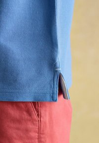 Sinise tekstuuriga polo särk külgvaheseintega, koos roosa lühikeste pükstega, millel on eesmine tasku. Särgi äärel on nähtavad õmblusaktsendid.