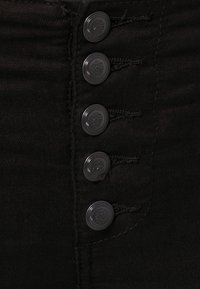 Mustekko mustasta denim-kankaasta, jossa on viisi metallista nappia ja ompeluyksityiskohtia. Nappit ovat pyöreitä, ja niissä on lievästi kiiltävä viimeistely.
