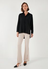 Black long-sleeve shirt with a collar and button closure, paired with beige fitted pants featuring front slits and pointed black and nude heels.