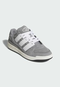 Gray sneaker with smooth and textured materials, white lace closure, three white stripes, and a rubber sole with subtle branding detail.