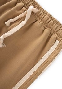 Braune Baumwollshorts mit einem gerafften Bund und einer cremefarbenen Kordel. Mit cremefarbenen Seitenstreifen und glatter Textur.