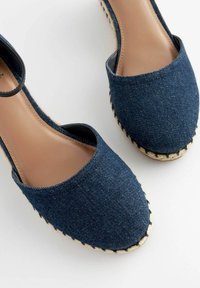 Espadrillas in denim con punta aperta, stoffa blu scuro, soletta beige e suola in juta con bordo intrecciato e cinturino alla caviglia.